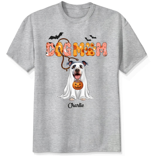 An ash grey t-shirt featuring a Halloween-themed graphic of a dog in a white ghost with a pumpkin, under the text 'DOG MOM' and custom with dog's name
