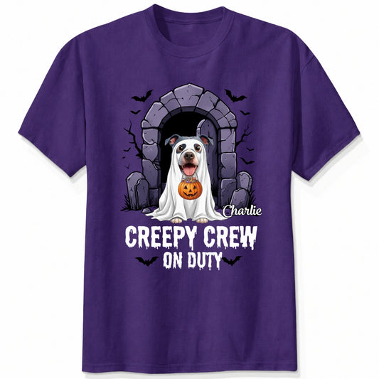 A custom purple t-shirt featuring a Halloween graphic of dogs in a ghost costume holding a pumpkin in front of a stone portal, with custom dog's names and the text 'CREEPY CREW ON DUTY' and small bat silhouettes.