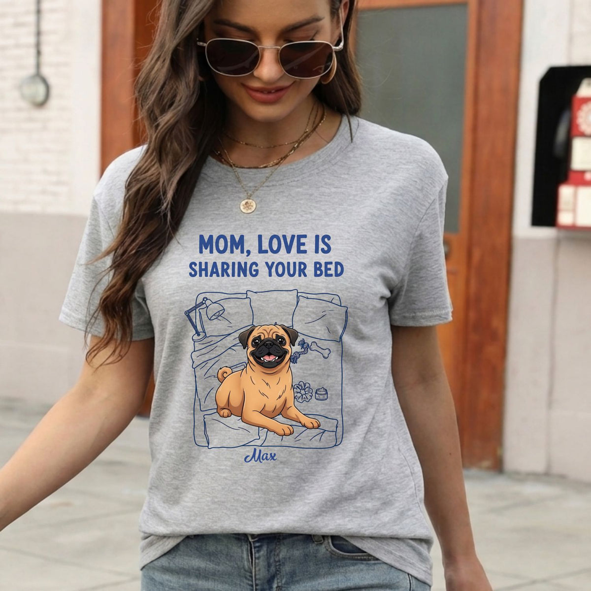 A woman wearing an ash gray graphic t-shirt with a pug dog illustration and the text 'MOM, LOVE IS SHARING YOUR BED'.