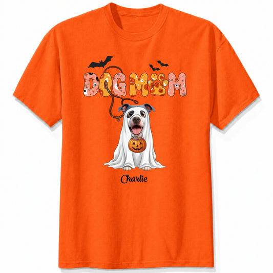 An orange t-shirt featuring a Halloween-themed graphic of a dog in a white ghost with a pumpkin, under the text 'DOG MOM' and custom with dog's name