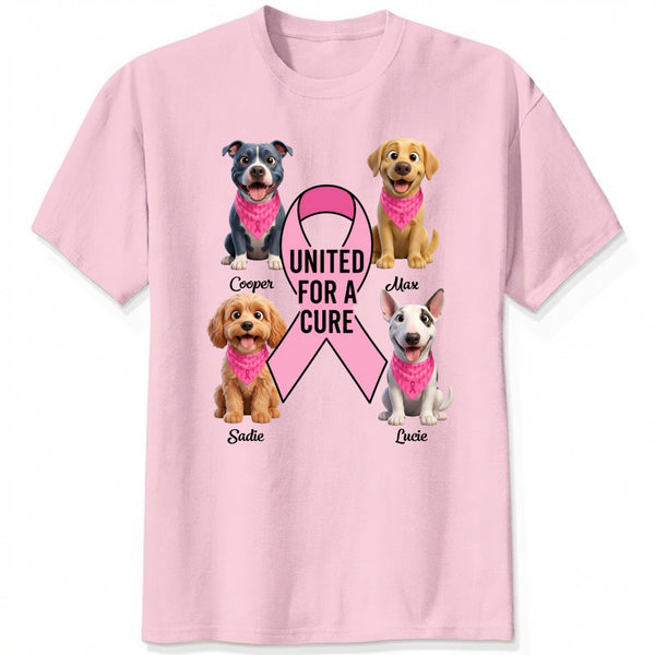 A light pink short-sleeve crewneck t-shirt featuring a graphic print of dogs wearing pink bandanas around a large pink ribbon with the text 'UNITED FOR A CURE'.
