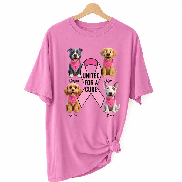 A pink short-sleeve t-shirt hanging on a wooden hanger against a white background, featuring a graphic of dogs wearing pink bandanas around a pink ribbon with the text 'UNITED FOR A CURE'.
