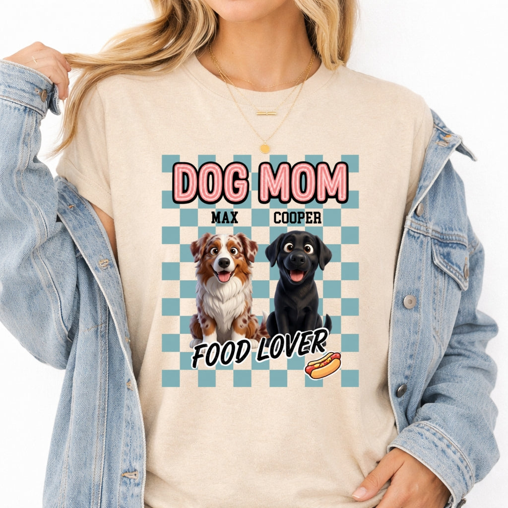 A woman wearing a sand t-shirt with a blue checkered design featuring two dogs and the text 'DOG MOM FOOD LOVER', styled with an open light blue denim jacket.