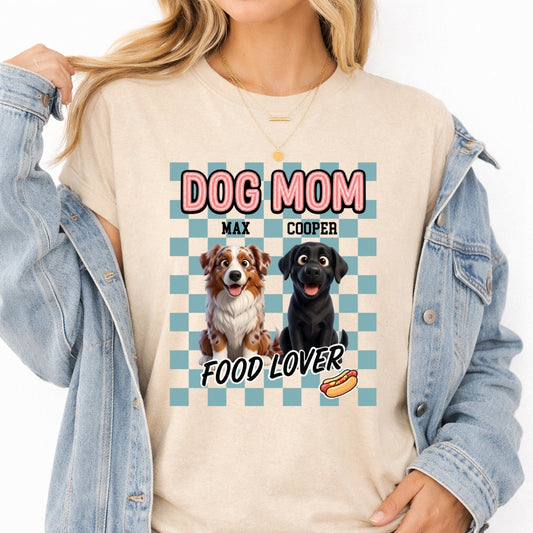 A woman wearing a sand t-shirt with a blue checkered design featuring two dogs and the text 'DOG MOM FOOD LOVER', styled with an open light blue denim jacket.