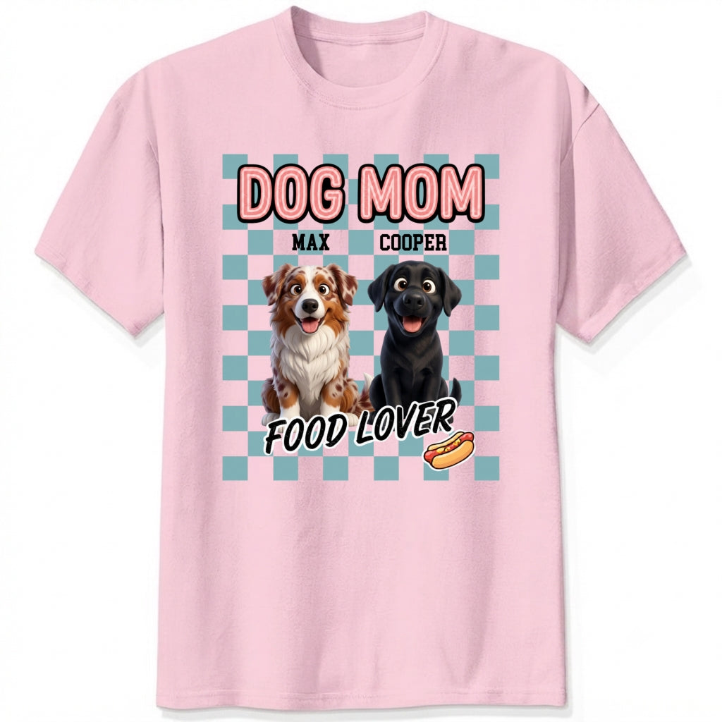 A pink short-sleeve t-shirt with a graphic print featuring custom dogs and the text 'DOG MOM FOOD LOVER' on a light blue checkerboard background.