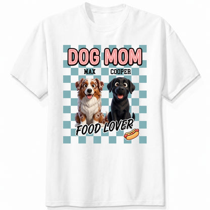 A white short-sleeve t-shirt with a graphic print featuring custom dogs and the text 'DOG MOM FOOD LOVER' on a light blue checkerboard background.