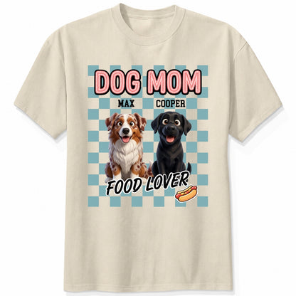 A sand short-sleeve t-shirt with a graphic print featuring custom dogs and the text 'DOG MOM FOOD LOVER' on a light blue checkerboard background.