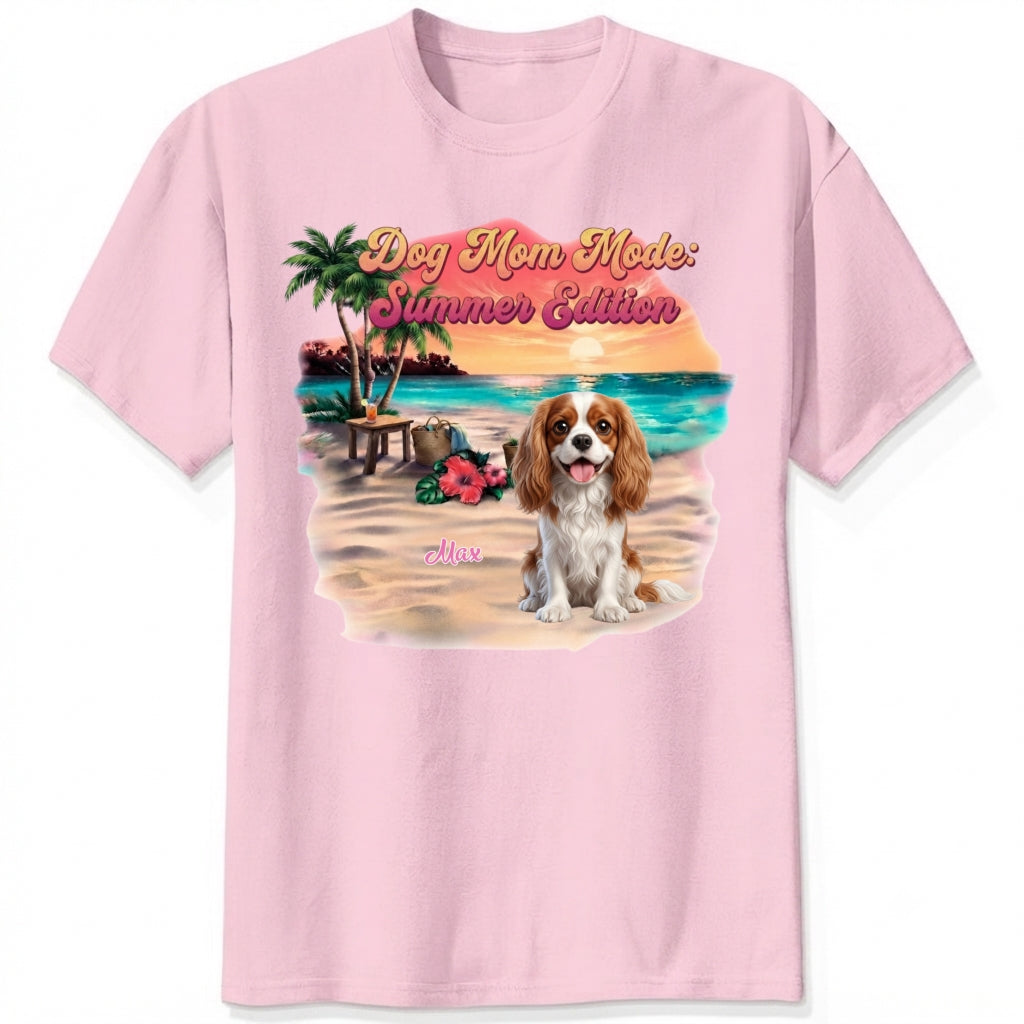 A pink short-sleeve crewneck t-shirt featuring a colorful graphic print of a dog on a beach with the text 'Dog Mom Mode: Summer Edition'. Personalized with a wide variety of dog breeds