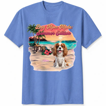 A blue short-sleeve crewneck t-shirt featuring a colorful graphic print of a dog on a beach with the text 'Dog Mom Mode: Summer Edition'. Personalized with a wide variety of dog breeds