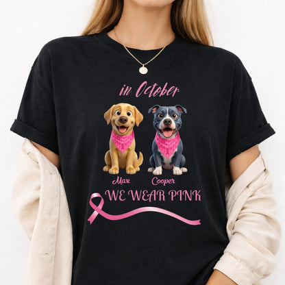 A woman wearing a black graphic T-shirt with pink text reading 'in October WE WEAR PINK' and two dogs wearing pink bandanas. The photo is cropped from the neck to the hips against a light neutral background. Personalized with a wide variety of dog breeds