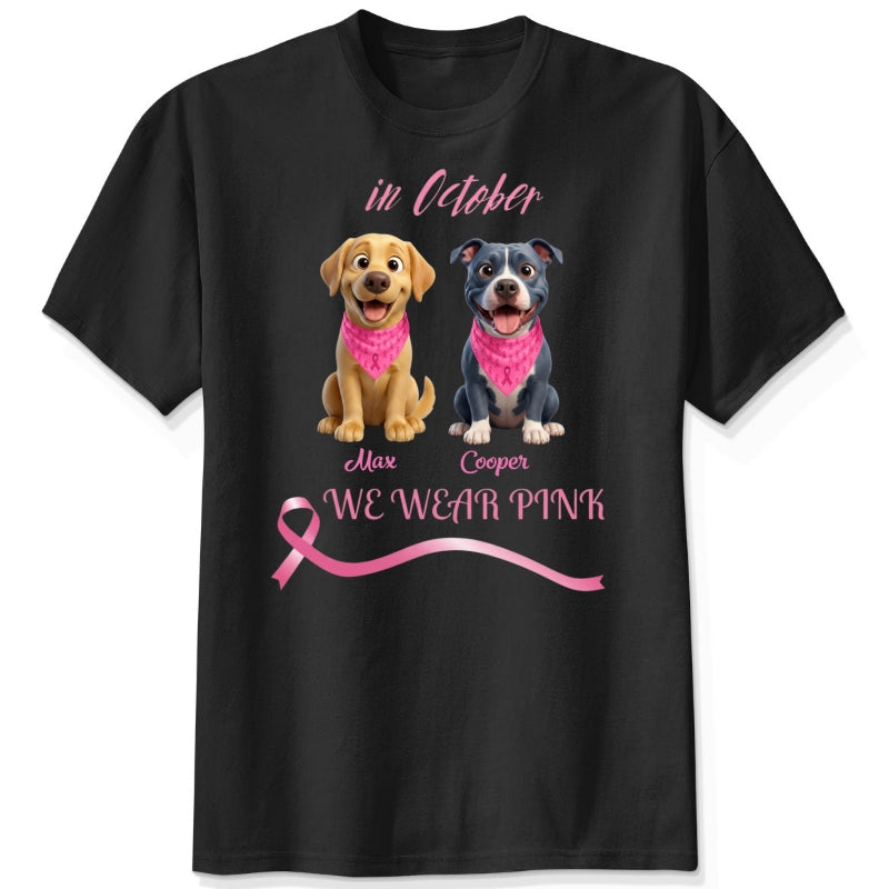 A black short-sleeve crewneck t-shirt featuring a graphic print of dogs wearing pink bandanas, with the text 'in October', 'WE WEAR PINK' along with a pink ribbon. Personalized with a wide variety of dog breeds