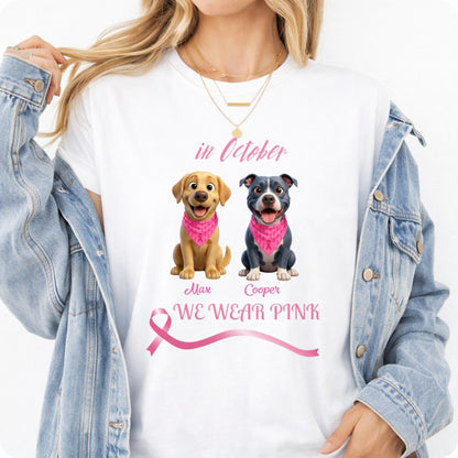 A woman wearing a white graphic T-shirt with a pink ribbon and two dogs, paired with an open light-wash denim jacket. The shirt reads 'in October WE WEAR PINK' with dogs wearing pink bandanas. Personalized with a wide variety of dog breeds