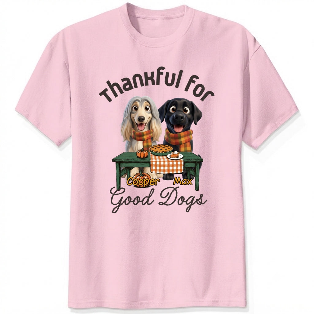 A pink short-sleeve crewneck t-shirt featuring a graphic print of custom dogs sitting at a table with autumn food, with the text 'Thankful for Good Dogs' and custom dog's names written around the illustration.