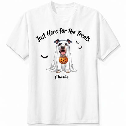 A white t-shirt featuring a cartoon graphic of a dog dressed in a white ghost holding a jack-o'-lantern, with the text 'Just Here for the Treats.' and custom with dog's name printed below