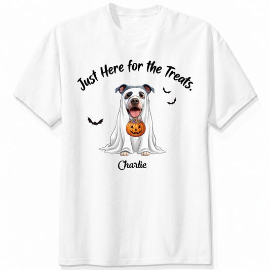 A white t-shirt featuring a cartoon graphic of a dog dressed in a white ghost holding a jack-o'-lantern, with the text 'Just Here for the Treats.' and custom with dog's name printed below
