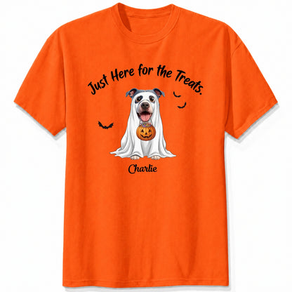 An orange t-shirt featuring a cartoon graphic of a dog dressed in a white ghost holding a jack-o'-lantern, with the text 'Just Here for the Treats.' and custom with dog's name printed below