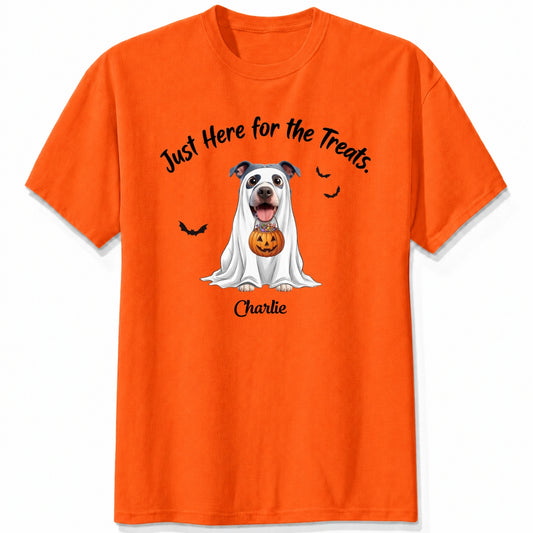 An orange t-shirt featuring a cartoon graphic of a dog dressed in a white ghost holding a jack-o'-lantern, with the text 'Just Here for the Treats.' and custom with dog's name printed below