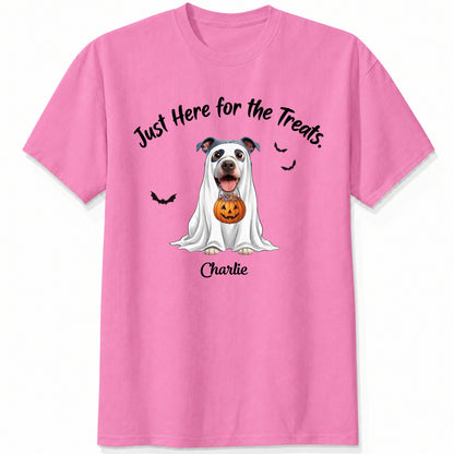 A pink t-shirt featuring a cartoon graphic of a dog dressed in a white ghost holding a jack-o'-lantern, with the text 'Just Here for the Treats.' and custom with dog's name printed below