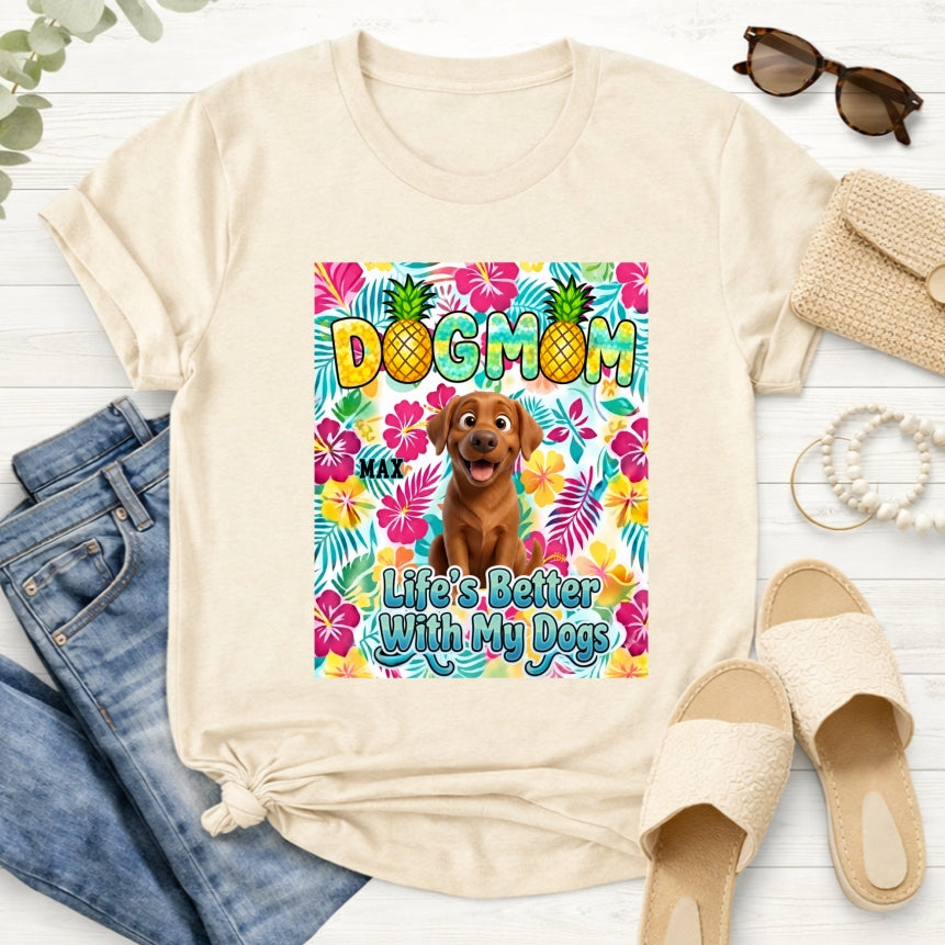 Asand custom dogs short-sleeve t-shirt featuring a colorful front graphic with the text 'DOG MOM' and 'Life's Better With My Dogs' alongside a cartoon dog and tropical floral background. The t-shirt is styled in a flat-lay arrangement with blue jeans, beige slide sandals, sunglasses, a burlap clutch, and a rope on a white wood background.