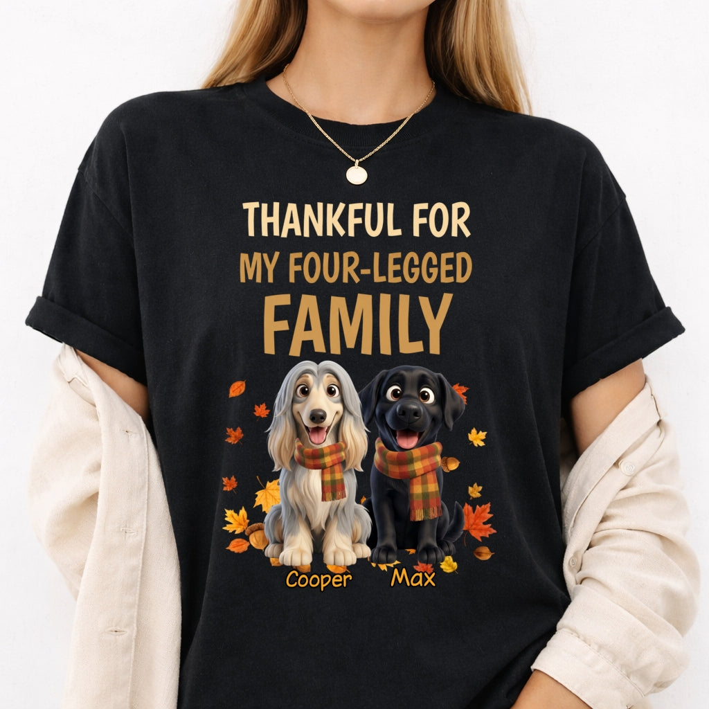 A woman wearing a black graphic t-shirt with a custom design that reads 'THANKFUL FOR MY FOUR-LEGGED FAMILY' above two dogs, wearing orange plaid scarves with autumn leaves. She has a cream-colored cardigan draped off her shoulders.