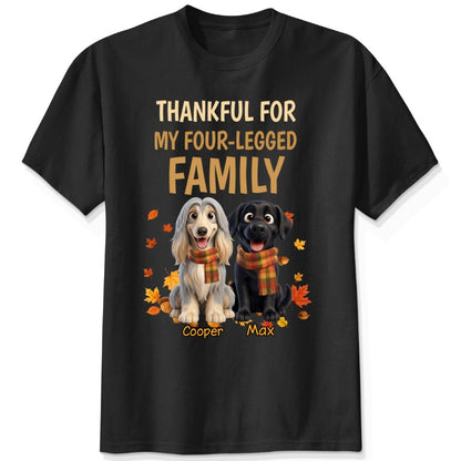 A black short-sleeve crewneck t-shirt with a graphic print. The print features the text 'THANKFUL FOR MY FOUR-LEGGED FAMILY' in beige and orange lettering, above an illustration of custom dogs wearing orange plaid scarves, surrounded by autumn leaves. customized with dog's names