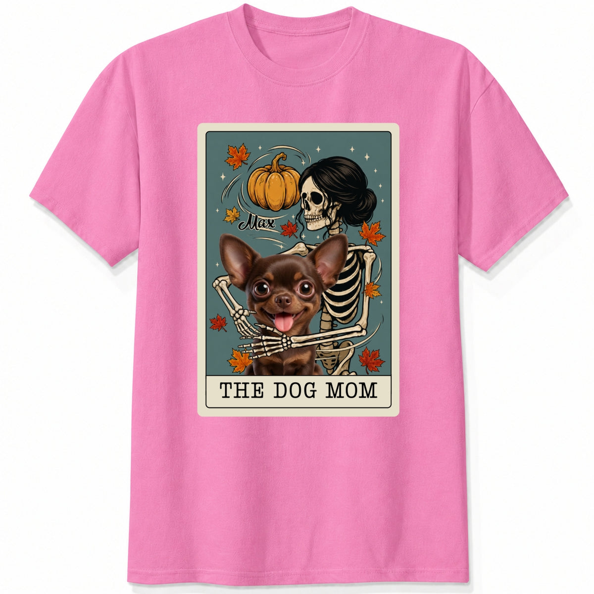 A pink short-sleeve crewneck t-shirt featuring a graphic print of a skeleton dog mom and a custom dog under a autumn pumpkin, styled like a tarot card labeled 'THE DOG MOM'.