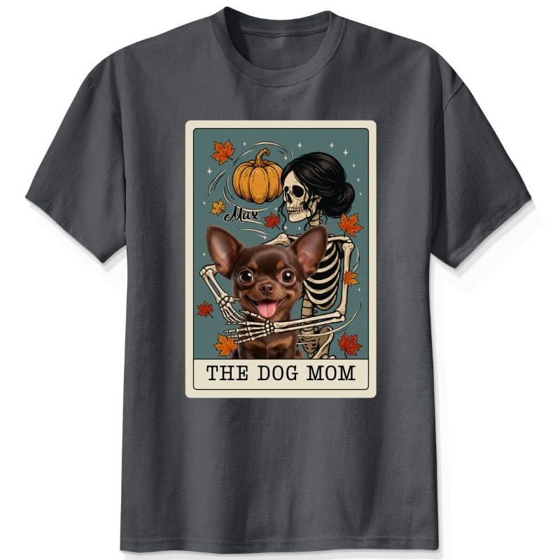 A dark gey short-sleeve crewneck t-shirt featuring a graphic print of a skeleton dog mom and a custom dog under a autumn pumpkin, styled like a tarot card labeled 'THE DOG MOM'.
