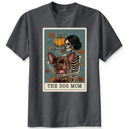 A dark gey short-sleeve crewneck t-shirt featuring a graphic print of a skeleton dog mom and a custom dog under a autumn pumpkin, styled like a tarot card labeled 'THE DOG MOM'.