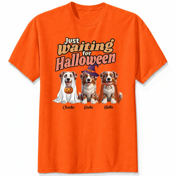 An orange short-sleeve crewneck t-shirt featuring dogs dressed in costumes and the text 'Just Waiting for Halloween'.